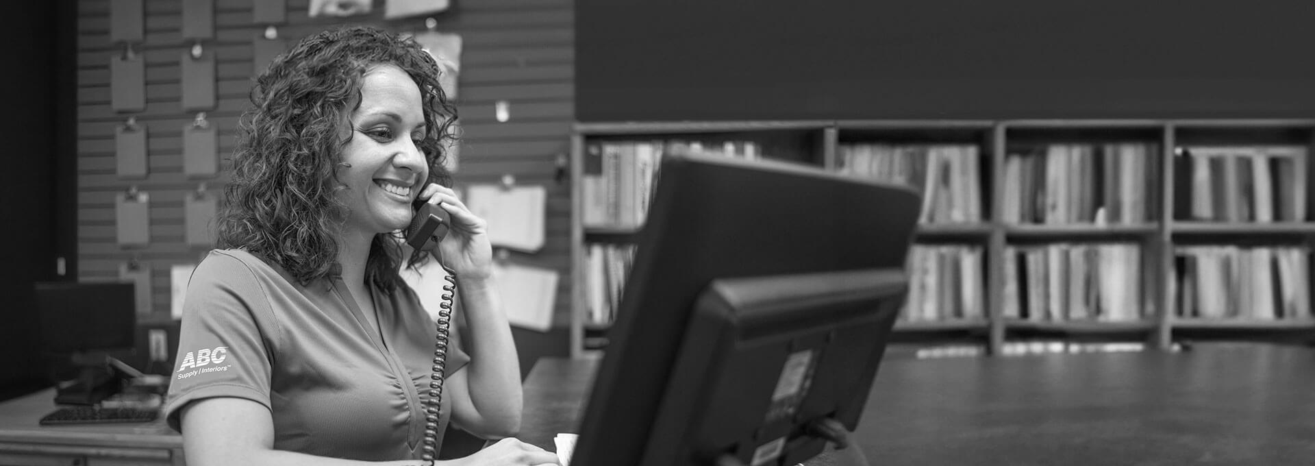 A smiling woman on the phone in front of a computer at a L&W Supply branch location.